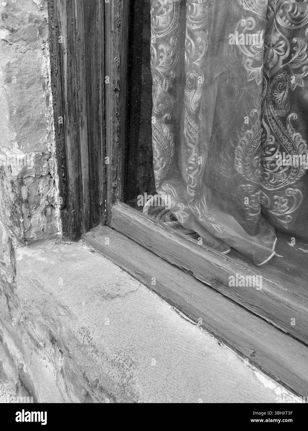 Guardando l'esterno di un vecchio edificio storico d'epoca si vede il primo piano di una facciata in mattoni di pietra con cornice in legno intorno alla finestra. Le tende sono un vecchio fascino. Foto Stock