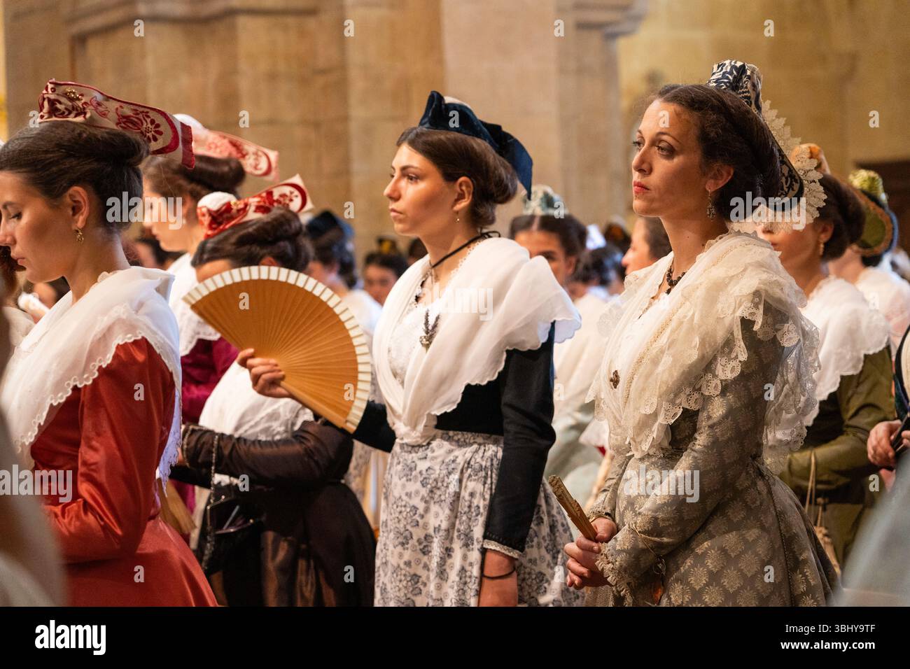 Le femmine che indossano abiti lunghi, scialli in pizzo e piccoli cappelli Arlesiani che rappresentano la loro regione in Provenza partecipano a una cerimonia religiosa all'inizio del t Foto Stock