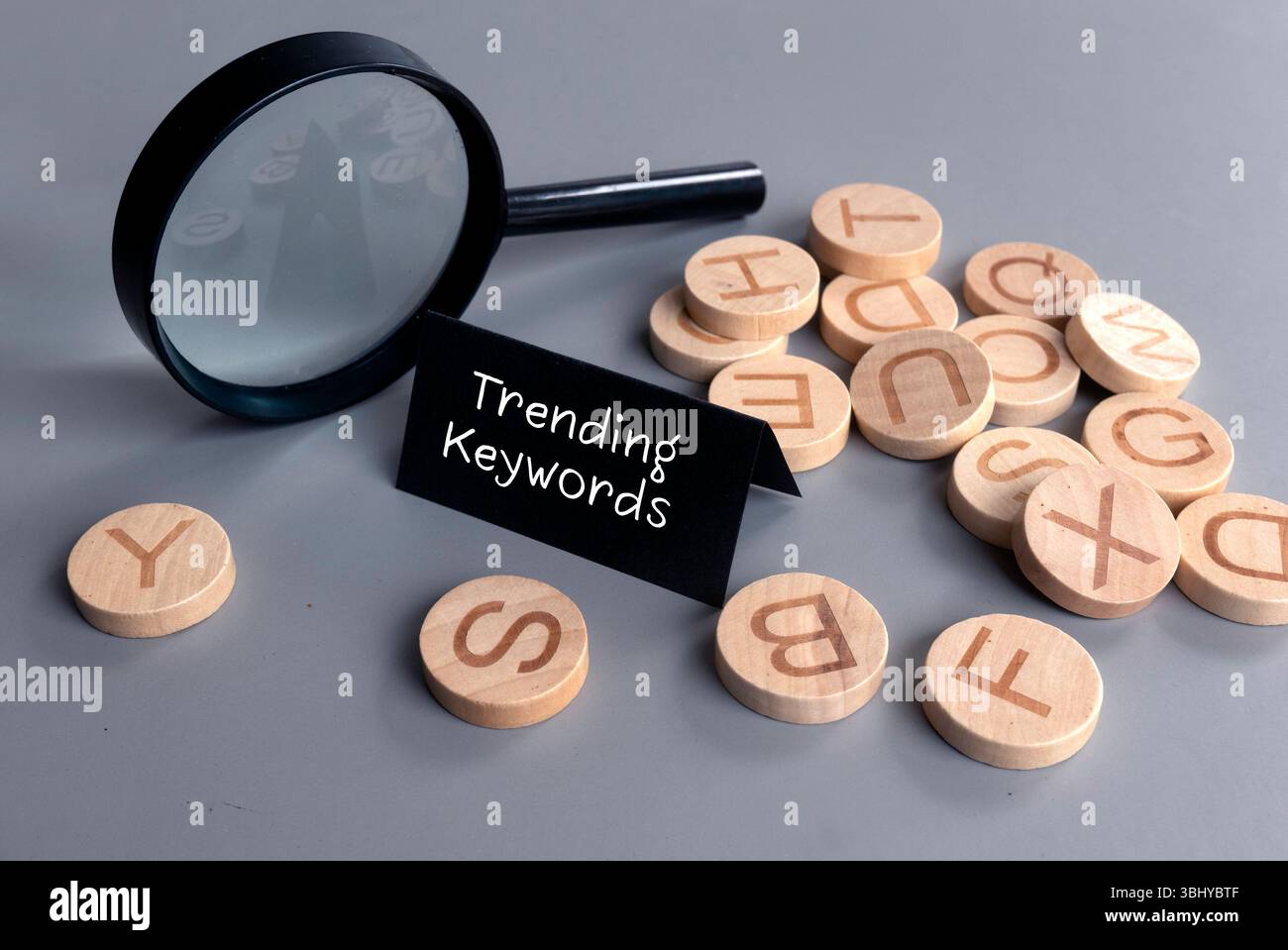 Lente d'ingrandimento e dischi alfabetici in legno con il simbolo "Trending Keywords" Foto Stock