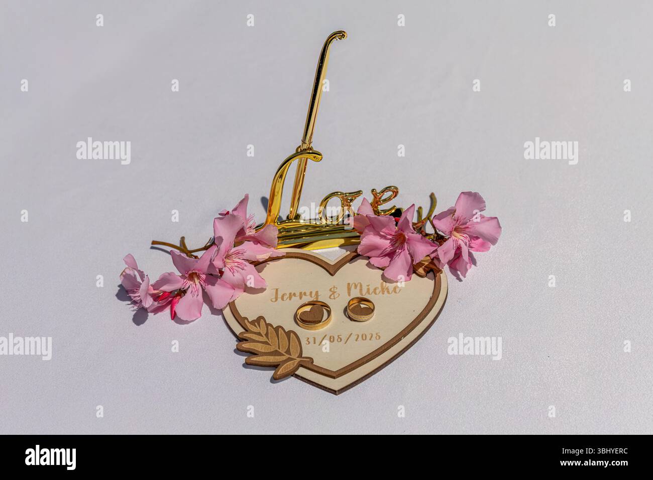 Placca nuziale in legno a forma di cuore con segno d'amore dorato e fiori rosa su sfondo bianco Foto Stock