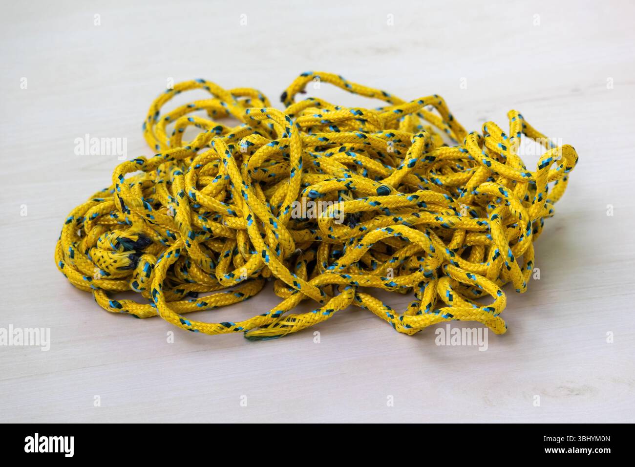 Una bobina di corda colorata disordinata ma resistente si appoggia su una superficie in legno. Questa fune intrecciata è adatta per l'asciugatura di stoffe domestiche, per legare oggetti e. Foto Stock