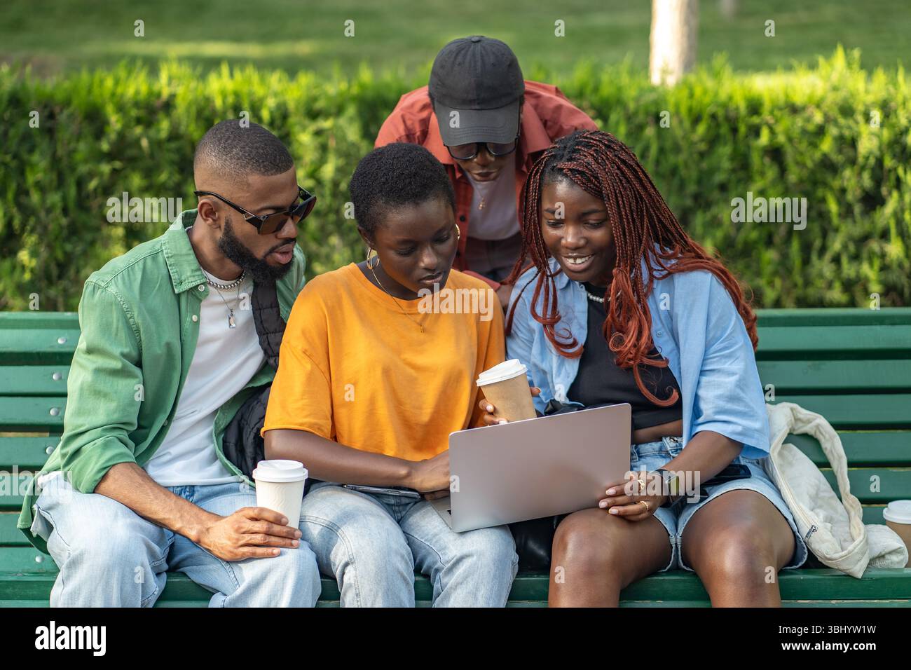 Allegro gruppo di amici afroamericani che bevono caffè e lavorano su computer portatili nel parco verde Foto Stock