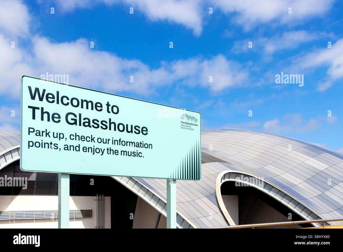 Cartello con la scritta "Welcome to the Glasshouse" con moderna struttura architettonica del Sage sullo sfondo sotto un cielo blu newcastle upon tyne, Regno Unito Foto Stock