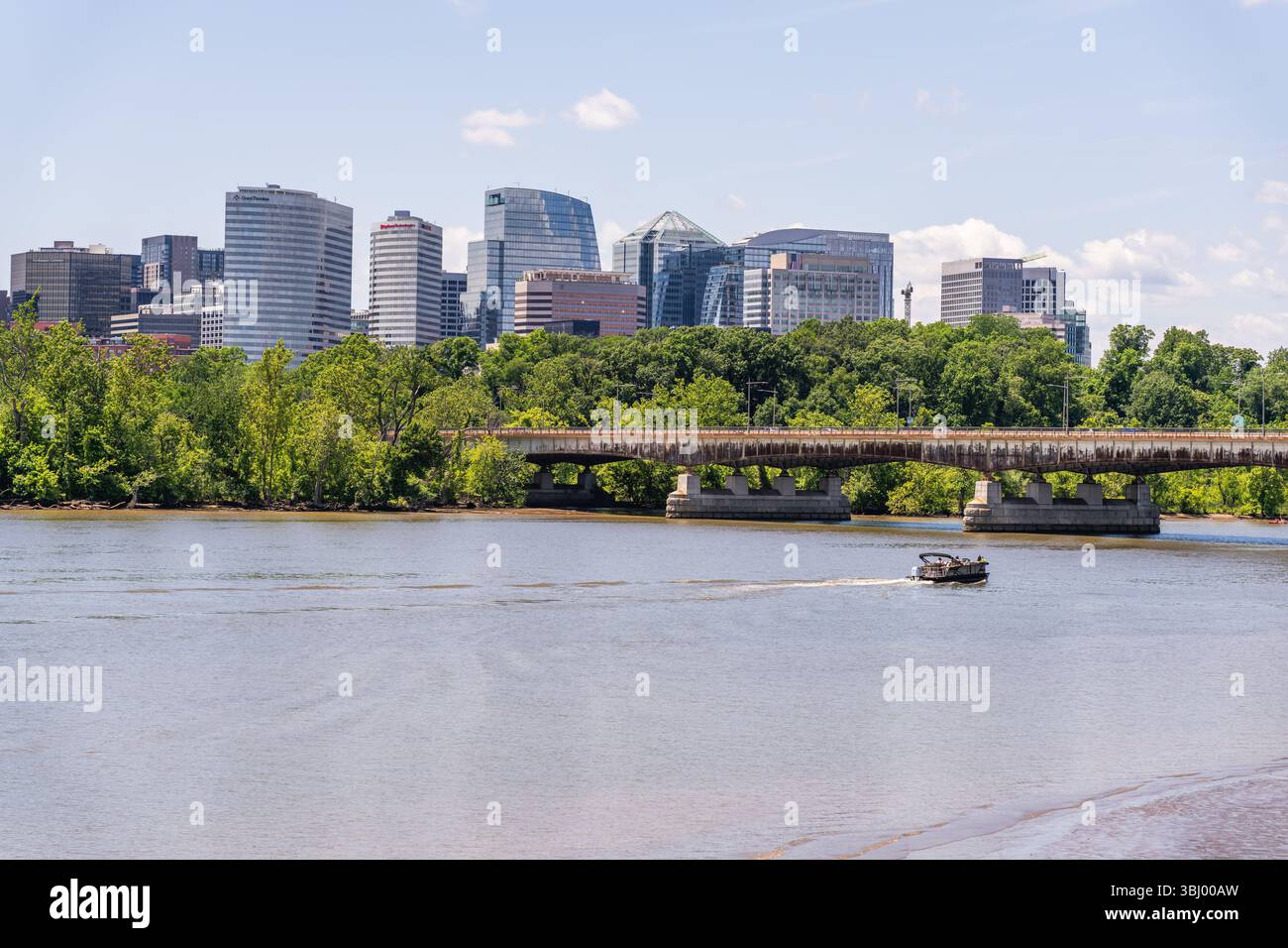Arlington, Virginia, USA, 26 maggio 2025. Una piccola barca naviga sul fiume Potomac con lo skyline moderno di Arlington e Key Bridge sullo sfondo Foto Stock