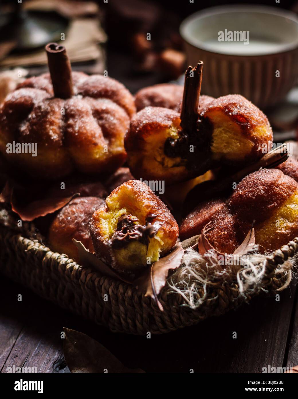 Un cestino accogliente pieno di ciambelle fatte in casa a forma di zucca, guarnite con zucchero e un tocco di cannella. L'ambiente caldo e invitante è perfetto per Foto Stock