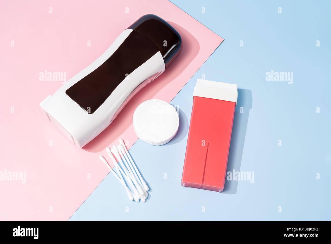 Stesa piatta di rotolo su materiale cerato su sfondo rosa pastello e blu. Dotato di scalda paraffina, cartuccia, tamponi di cotone e bastoncini di cotone, ideale per il beaut Foto Stock
