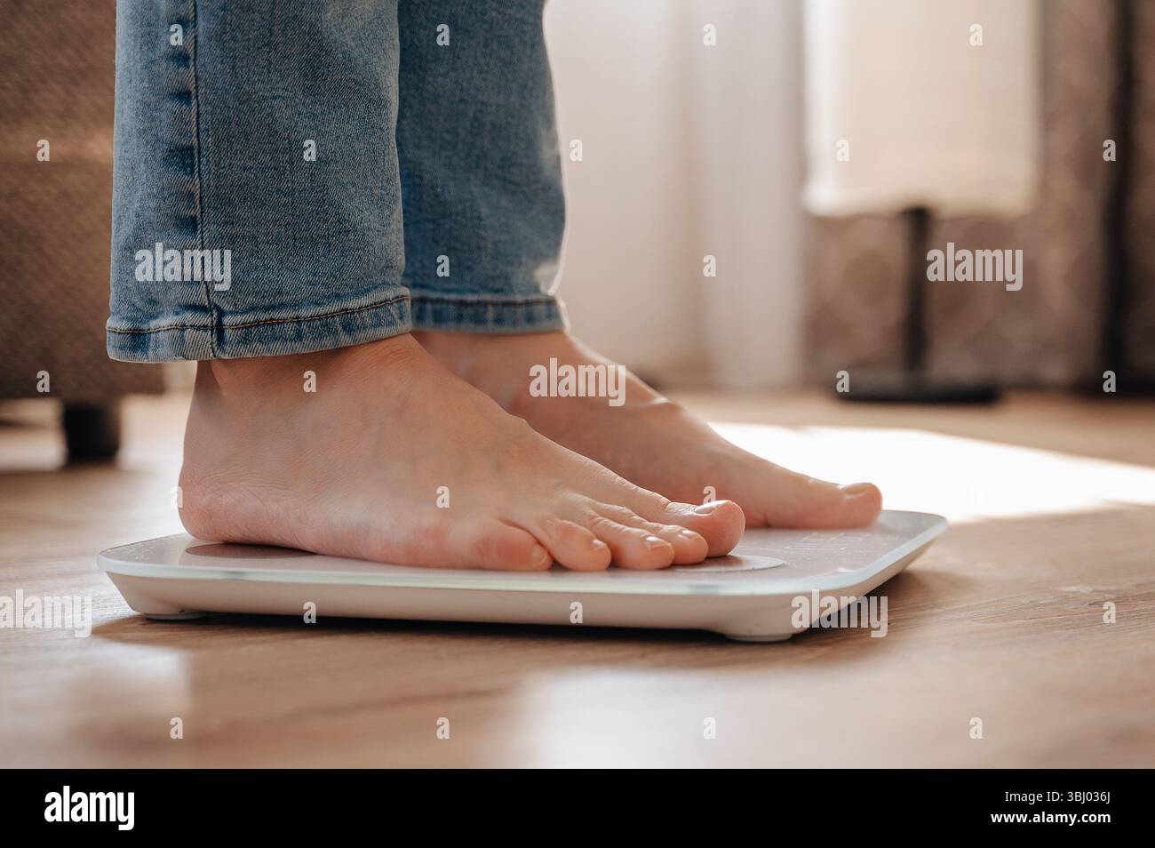 Una giovane donna sta su una bilancia a casa, sottolineando un viaggio personale di perdita di peso. L'immagine cattura il concetto di consapevolezza della salute, obiettivi di fitness, Foto Stock