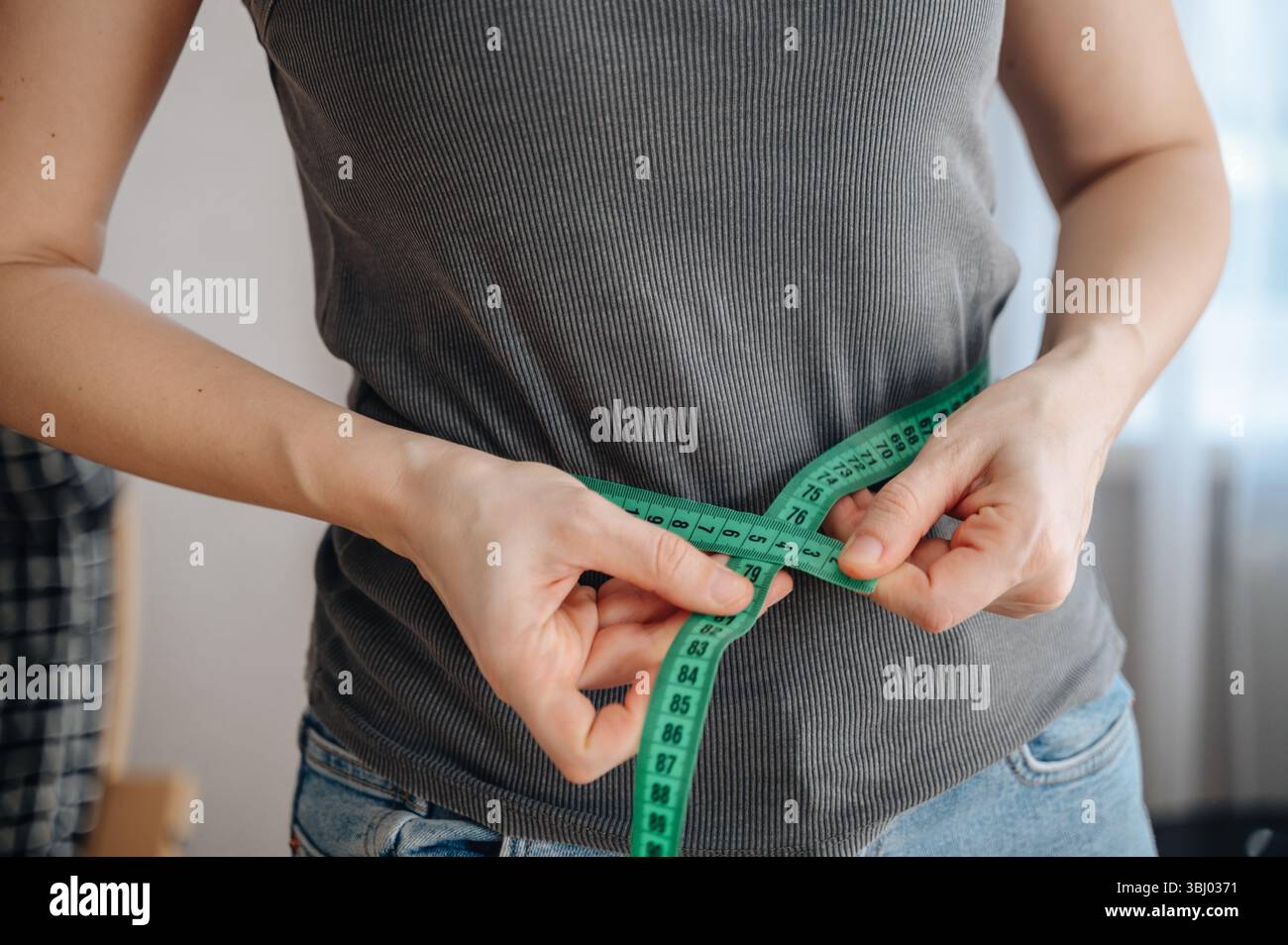 Una donna misura la vita con un metro a nastro verde, simboleggiando il suo percorso di perdita di peso. Indossa un outfit casual, incarnando l'impegno per la salute Foto Stock