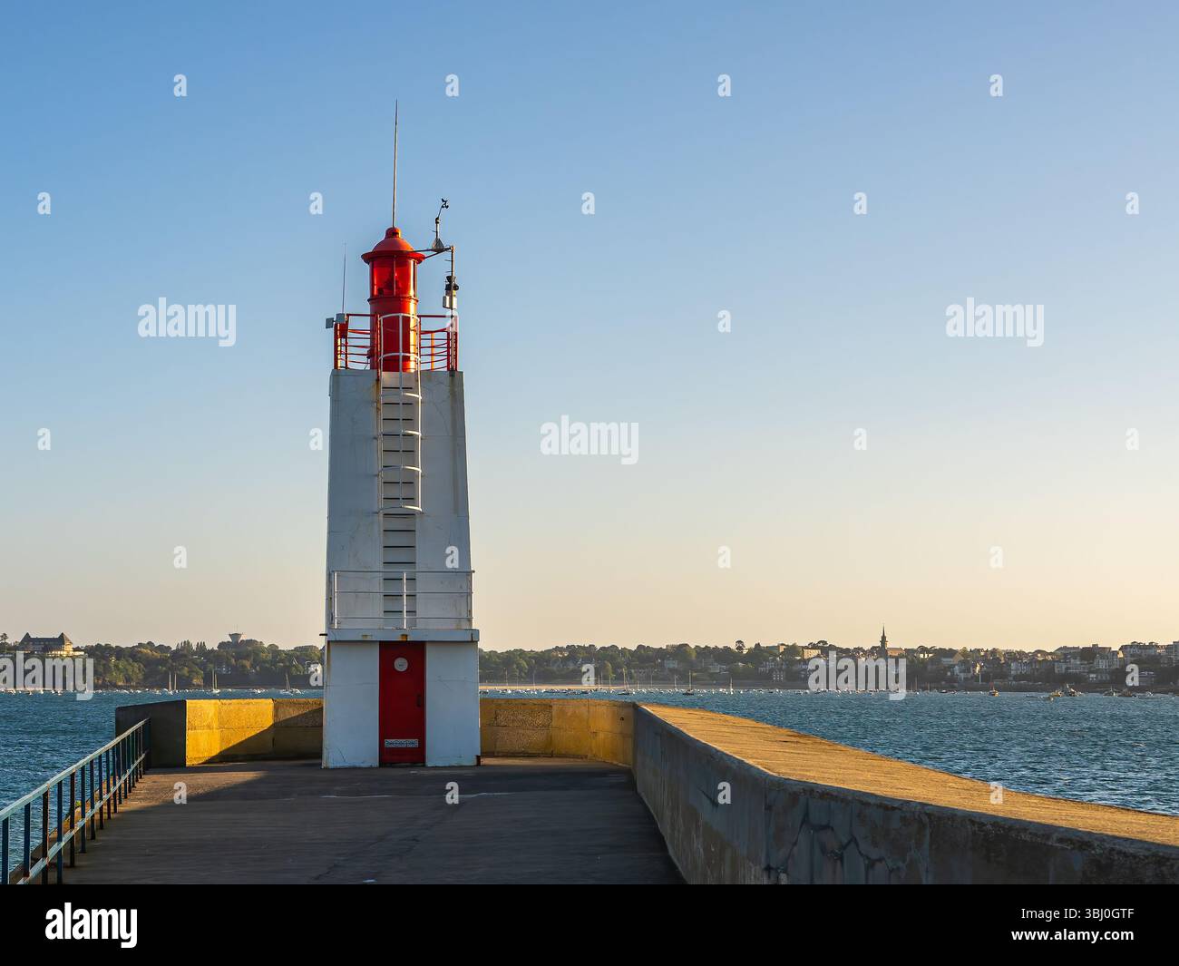 Faro rosso e bianco sul molo di Môle des Noires a Saint-Malo al tramonto. Luce serale sulla costa della Bretagna, in Francia, con mare e città nel bac Foto Stock