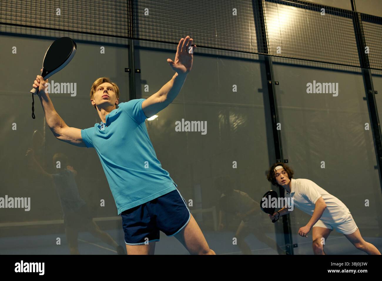 Due giovani sportivi mettono in mostra le loro abilità mentre giocano a padel in casa durante una partita competitiva. Foto Stock