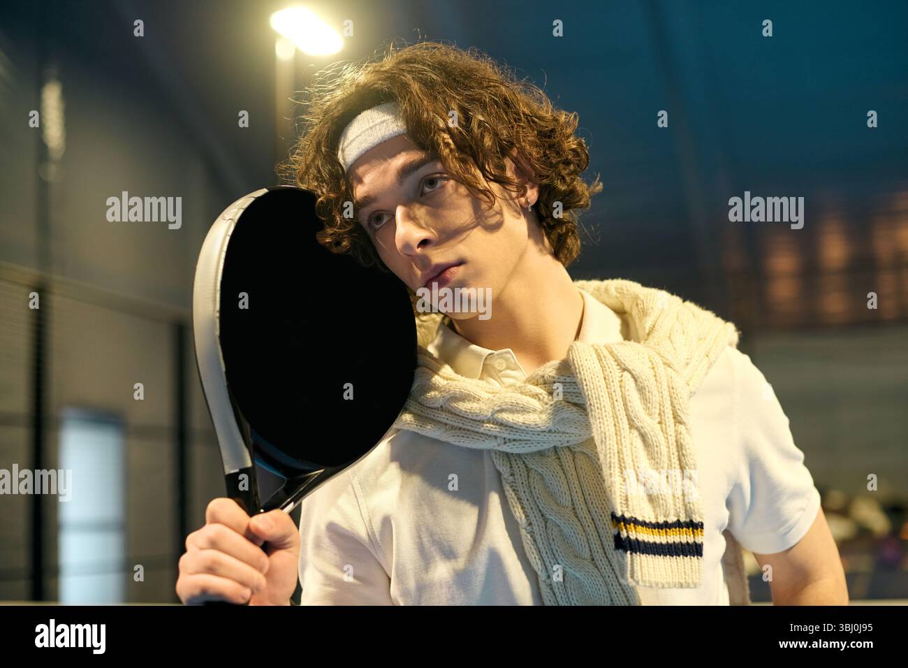 Un giovane indossa un abito elegante mentre gioca sapientemente a padel su un campo coperto. Foto Stock