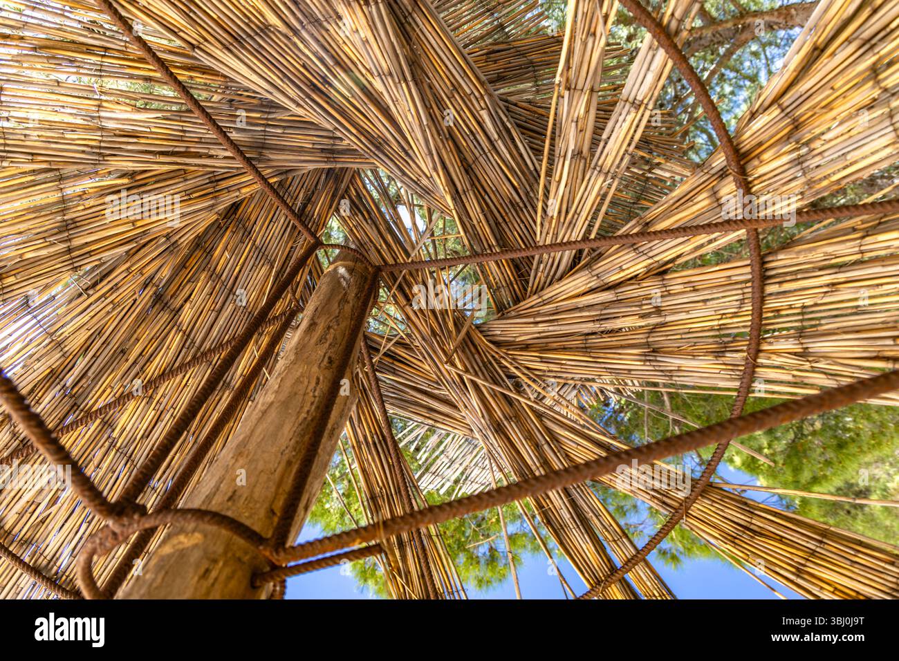 Un parasole in paglia distrutto sulla spiaggia, un molo sul fondo per la struttura e un ombrello strappato Foto Stock