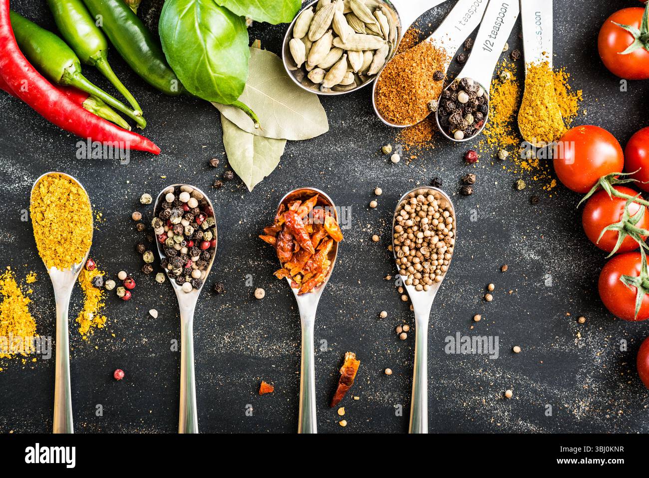 cucchiai con spezie e verdure diverse su un tavolo nero Foto Stock