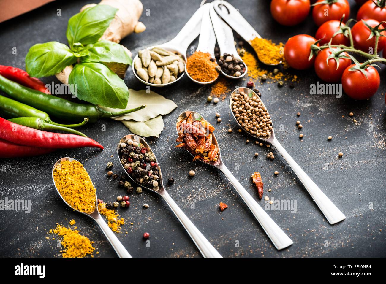 cucchiai con spezie e verdure diverse su un tavolo nero Foto Stock