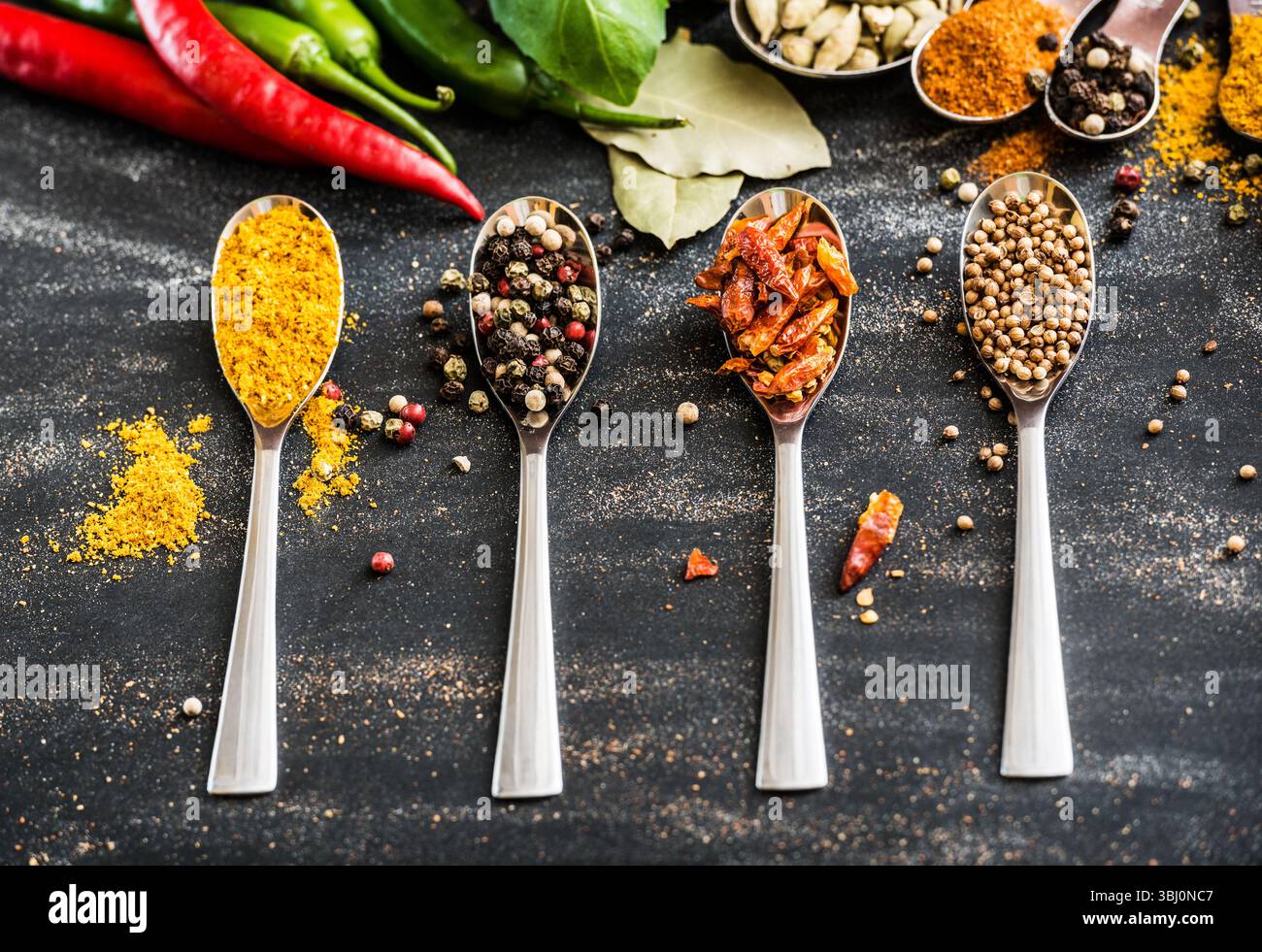 cucchiai con spezie e verdure diverse su un tavolo nero Foto Stock