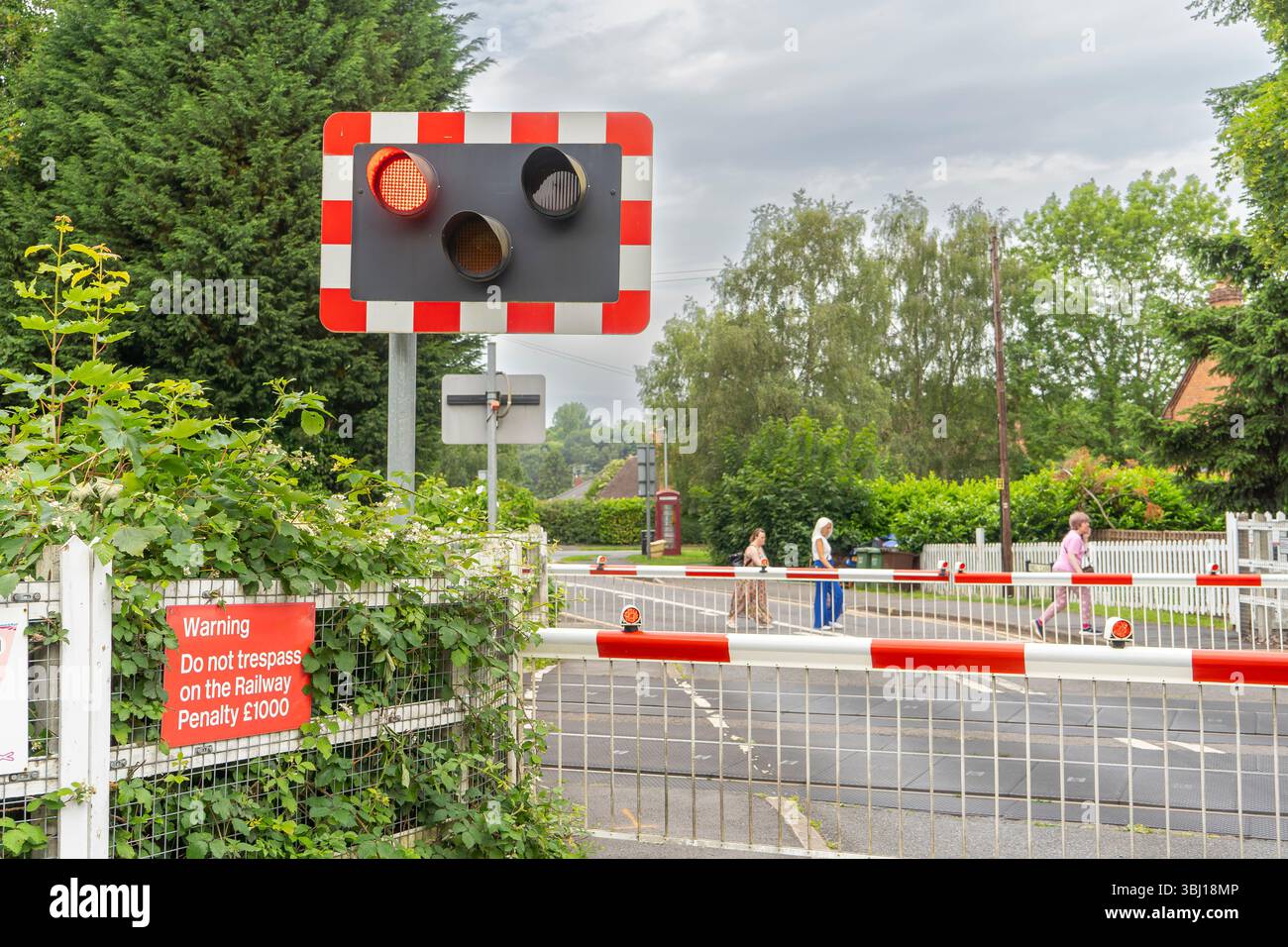 Passaggio a livello chiuso alla stazione ferroviaria di Blakedown con luci rosse lampeggianti e persone che camminano dietro la barriera. Foto Stock