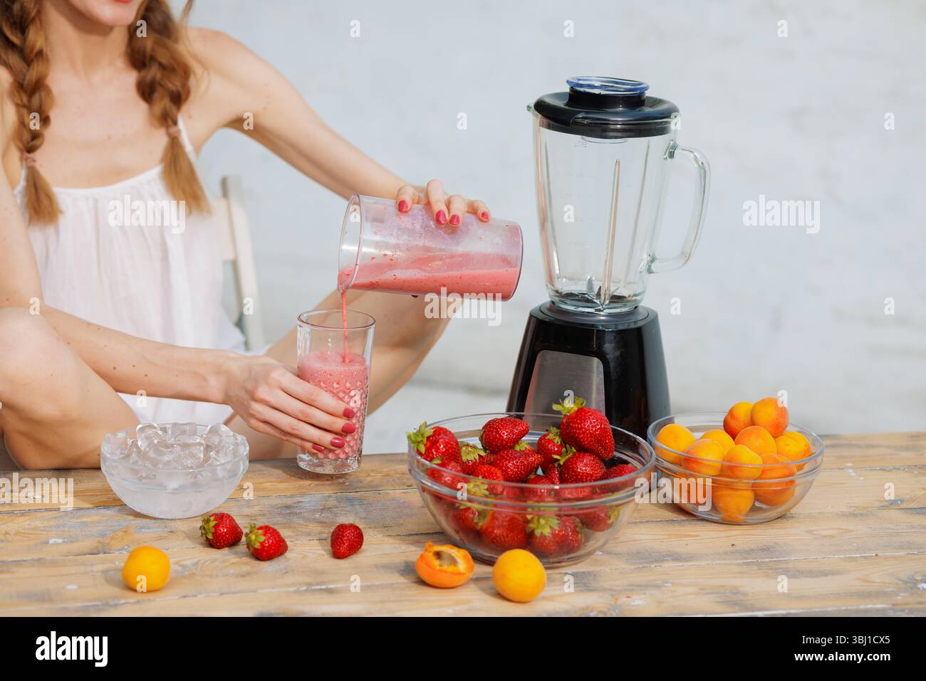 Frullato di fragole fatto in casa versato in un bicchiere su un tavolo rustico con frutta fresca e frullatore. Rinfresco estivo. Foto Stock