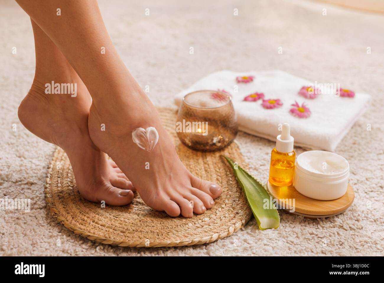 Crema per piedi a forma di cuore, aloe, olio, asciugamano e candela in un accogliente ambiente spa. Concetto di autocura naturale e idratazione della pelle. Foto Stock