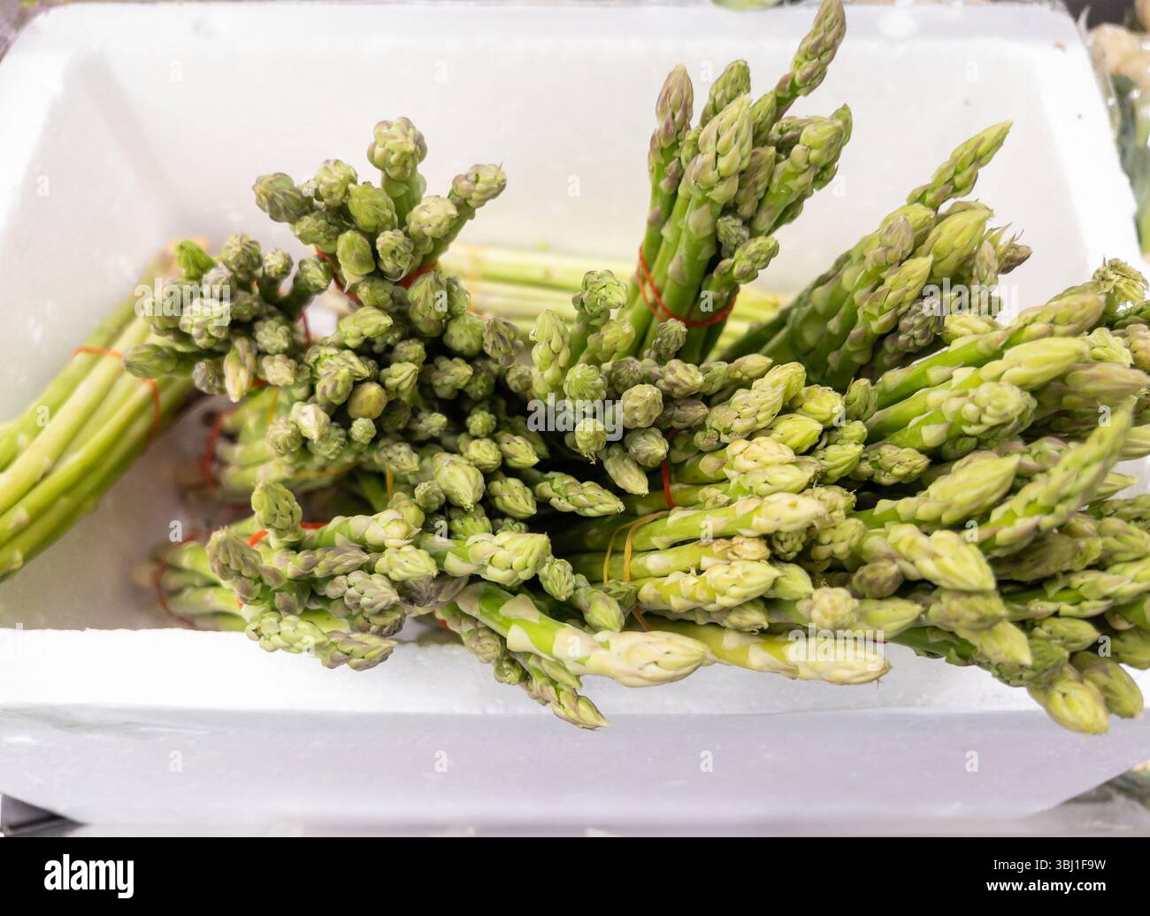 Asparagi verdi vivaci in una scatola di schiuma, esposti per la vendita in un mercato. Ideale per la spesa, l'agricoltura e la sana alimentazione di immagini stock. Foto Stock