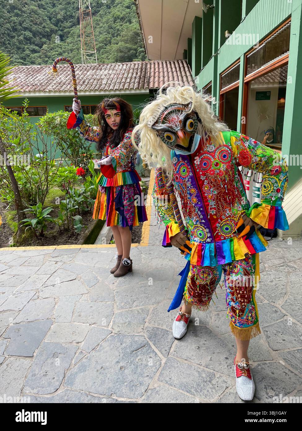 Due persone in costumi colorati si trovano di fronte a un edificio. Uno di loro ha in mano un bastone Foto Stock