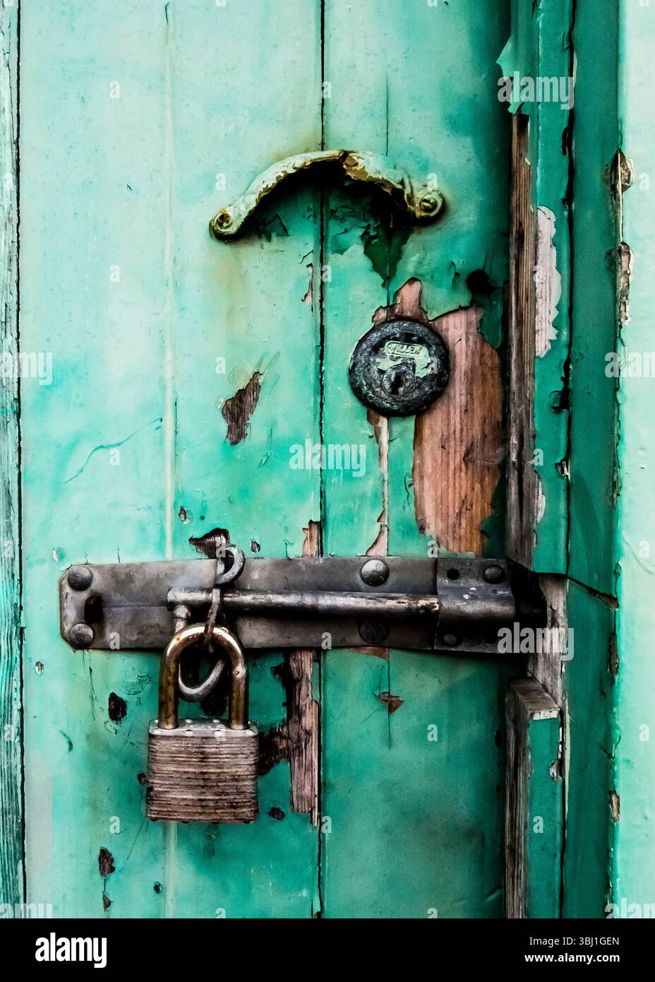Una foto ravvicinata di una porta in legno color acqua con una serratura arrugginita e una maniglia. Foto Stock
