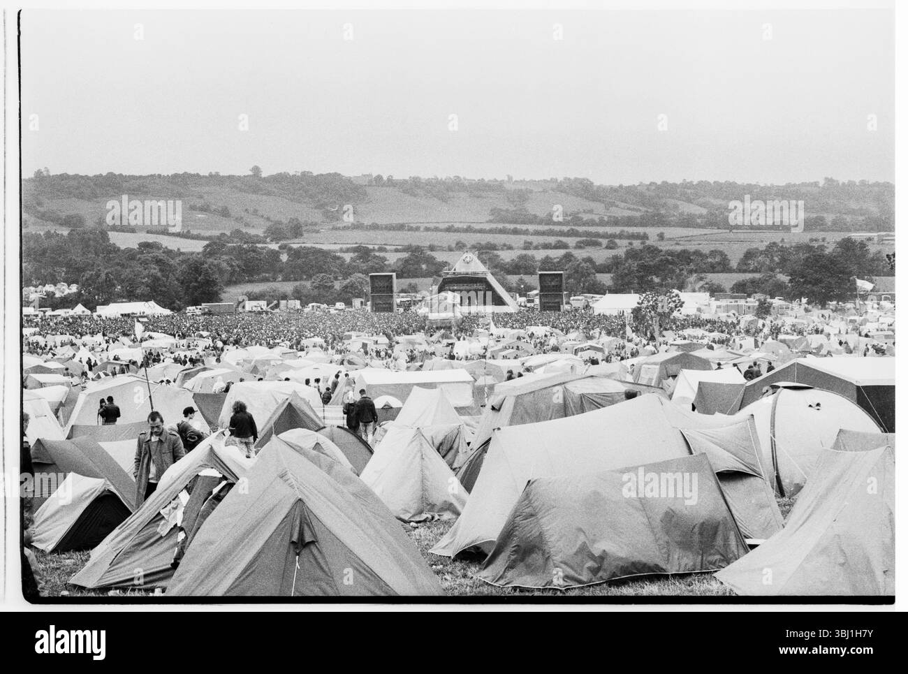 GLASTONBURY 1990, CAMPO PRINCIPALE, AMPIA VISTA: La vista dal retro del campo principale attraverso le tende e i camper verso il Pyramid Main Stage al Glastonbury Festival, Pilton Farm, Somerset, Inghilterra, giugno 1990. Nel 1990 il festival ha celebrato il suo ventesimo anniversario. A questo punto si poteva ancora accamparsi in fondo al campo principale. Non consentono più le tende sul retro del campo principale. Fotografia: ROB WATKINS Foto Stock