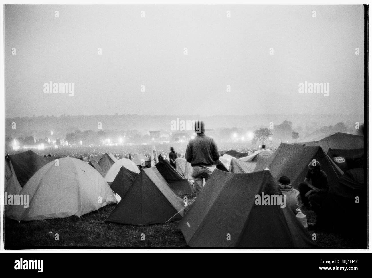 PALCO PIRAMIDALE, CAMPO PRINCIPALE, LOU REED, GLASTONBURY 92: La vista dal retro del Main Field mentre Lou Reed suona il Pyramid Stage al Glastonbury Festival, Pilton, Inghilterra, giugno 27 1992. La gente illuminava i bagliori e tutta la valle era piena di fumo, creando un'atmosfera spaventosa. A questo punto si poteva ancora accamparsi in fondo al campo principale. Non consentono più le tende sul retro del campo principale. Il festival è cresciuto così tanto che anche le colline vuote dietro il Pyramid Stage in questa foto sono ora parte del festival. Fotografia: ROB WATKINS Foto Stock