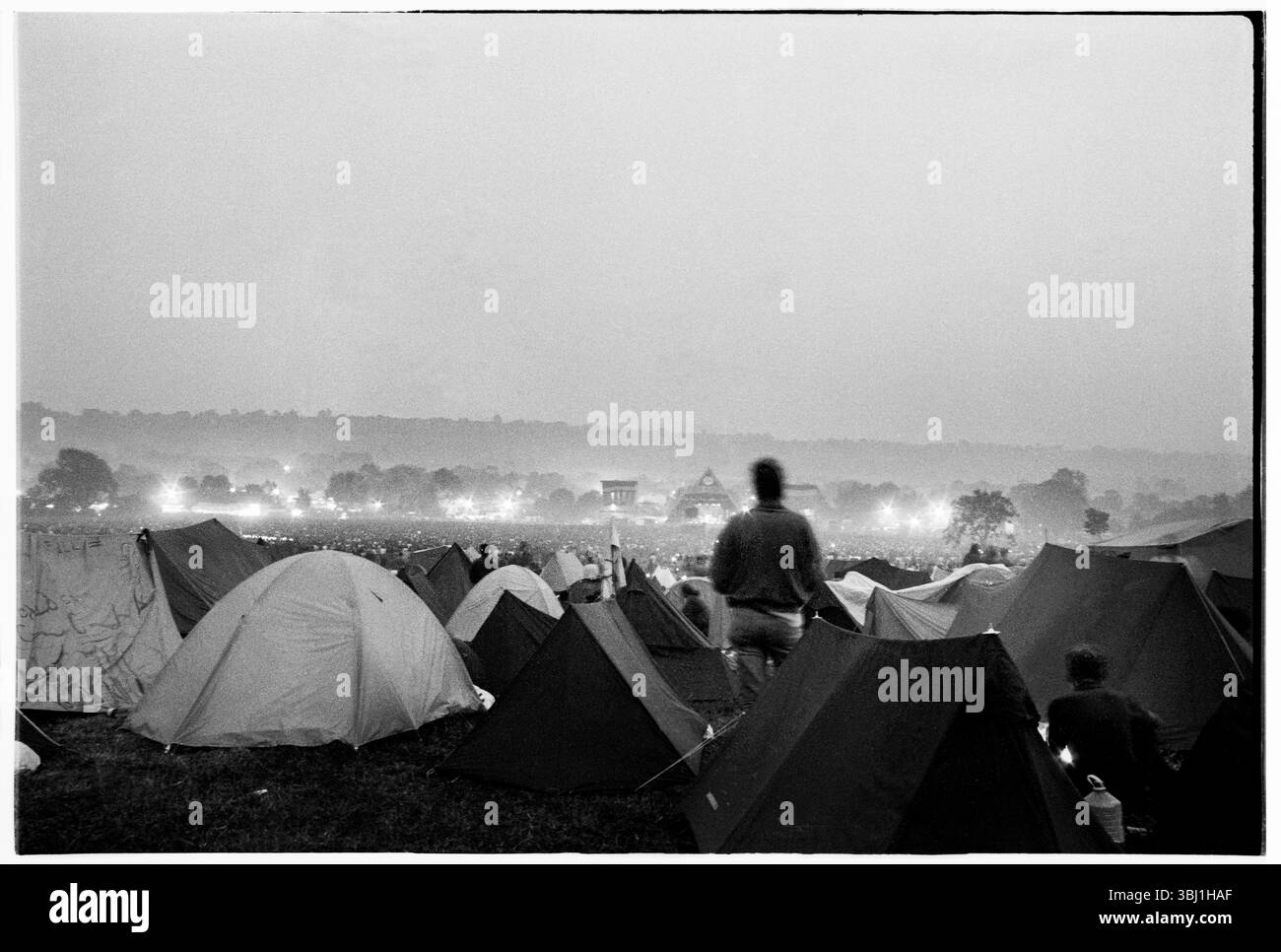 PALCO PIRAMIDALE, CAMPO PRINCIPALE, LOU REED, GLASTONBURY 92: La vista dal retro del Main Field mentre Lou Reed suona il Pyramid Stage al Glastonbury Festival, Pilton, Inghilterra, giugno 27 1992. La gente illuminava i bagliori e tutta la valle era piena di fumo, creando un'atmosfera spaventosa. A questo punto si poteva ancora accamparsi in fondo al campo principale. Non consentono più le tende sul retro del campo principale. Il festival è cresciuto così tanto che anche le colline vuote dietro il Pyramid Stage in questa foto sono ora parte del festival. Fotografia: ROB WATKINS Foto Stock