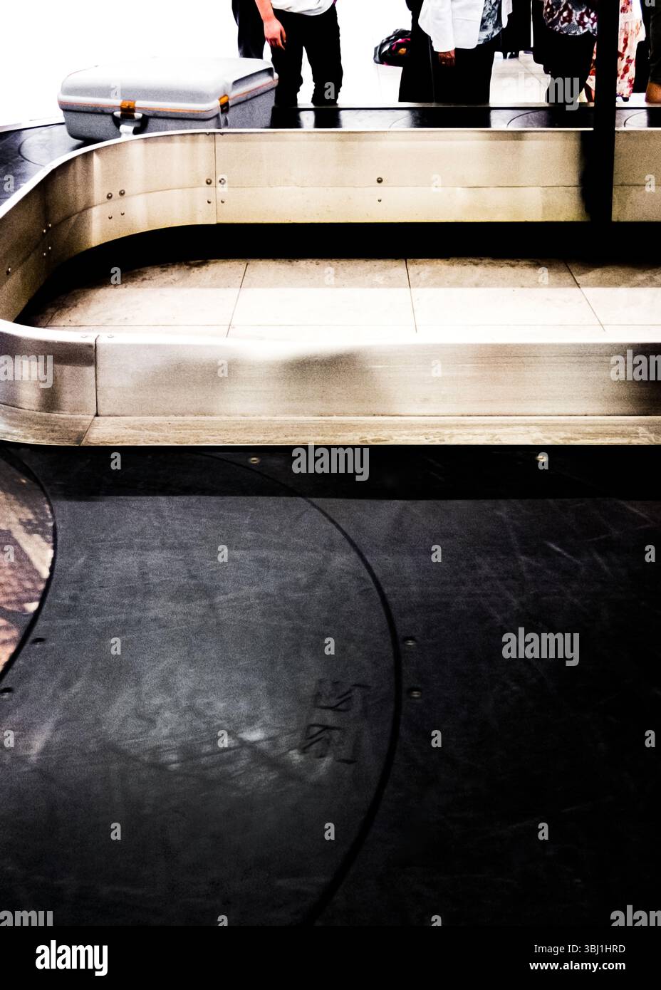 Una valigia si trova su una giostra bagagli, con persone in piedi nelle vicinanze. Foto Stock