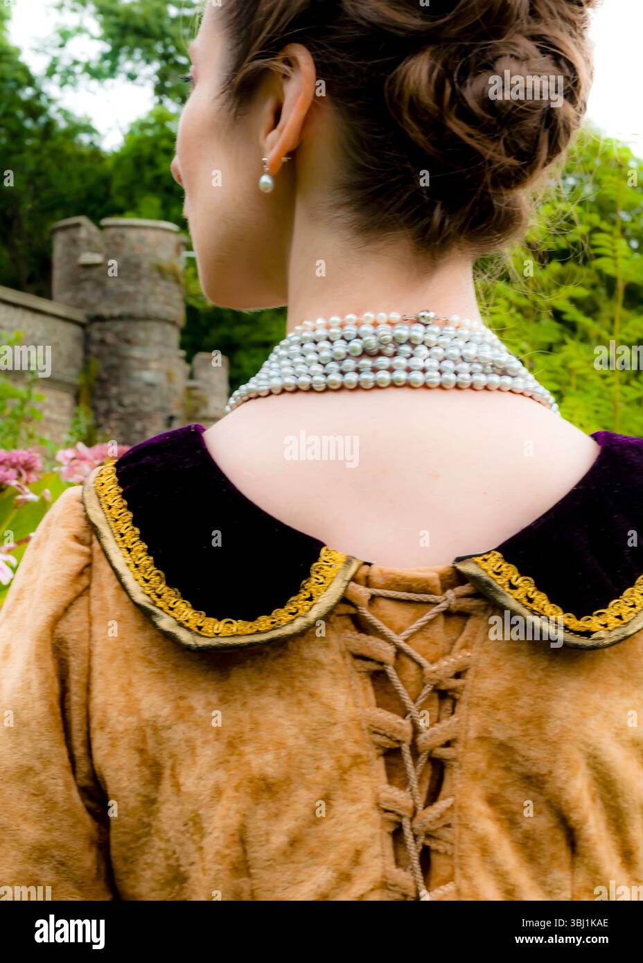Una donna in costume storico, con una collana di perle e orecchini, si erge all'aperto. Foto Stock