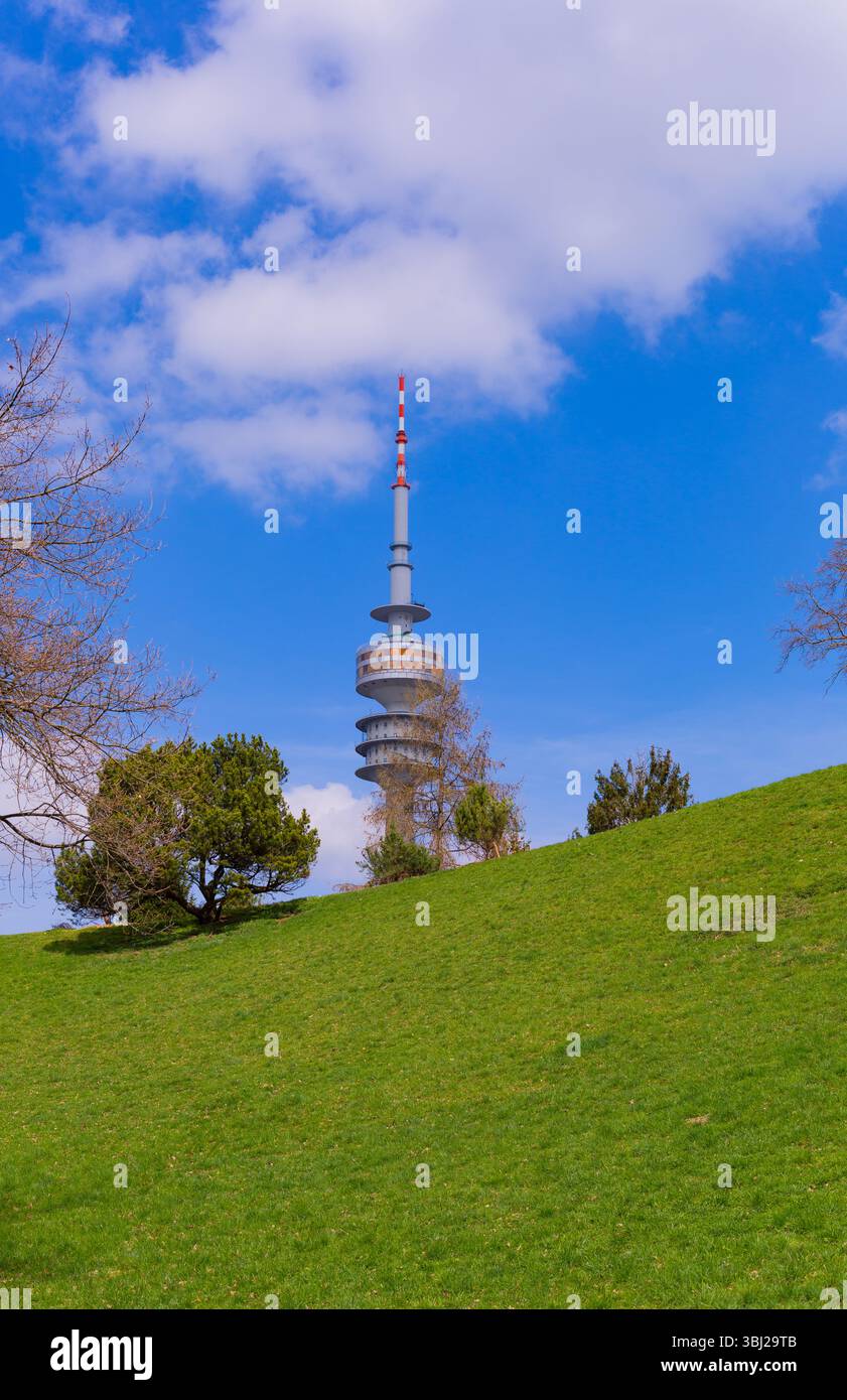 Monaco di Baviera, Germania - 2 aprile 2025: Olympiaturm (torre Olympia) al parco Olympia. Guardando in alto attraverso gli alberi del parco. Costruito per la partita olimpica Foto Stock