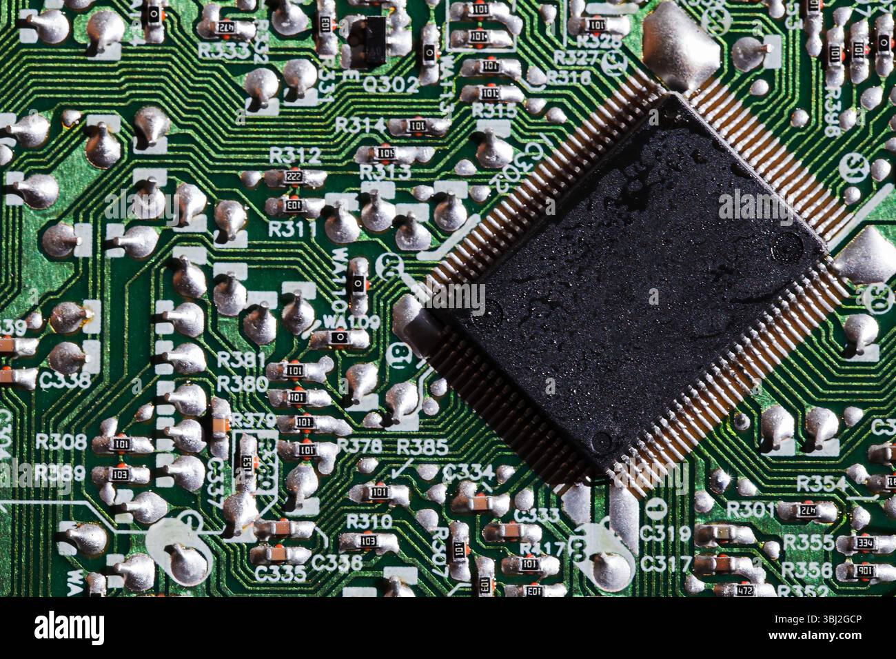 Immagine dettagliata che mostra un microchip saldato su una complessa scheda elettronica verde, che sottolinea la complessità e la precisione della tecnologia moderna Foto Stock