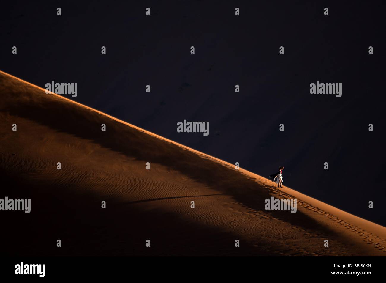 Una figura solitaria è ambientata in scala nelle grandi dune di sabbia rossa di Sossusvlei, Namib Naukluft National Park, Namibia all'alba. Foto Stock