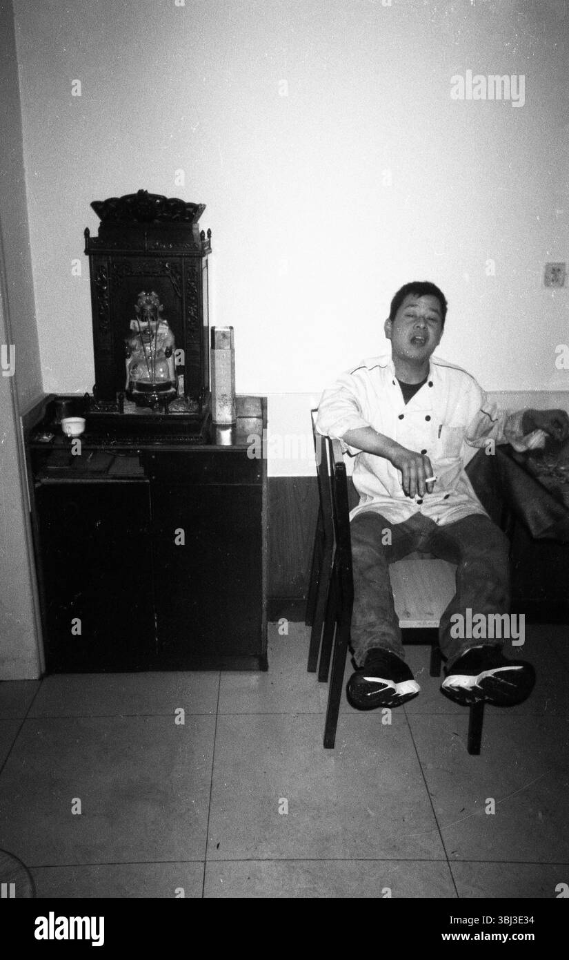 Chef Tianjin della fine degli anni '2000 che fuma accanto al santuario God of Wealth, foto documentario in bianco e nero Foto Stock