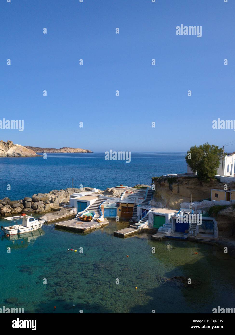 Scogliere e tradizionali capanne da pesca di Mandrakia sotto il sole luminoso. Il mare turchese contrasta con le facciate bianche e le vivaci texture costiere. Foto Stock