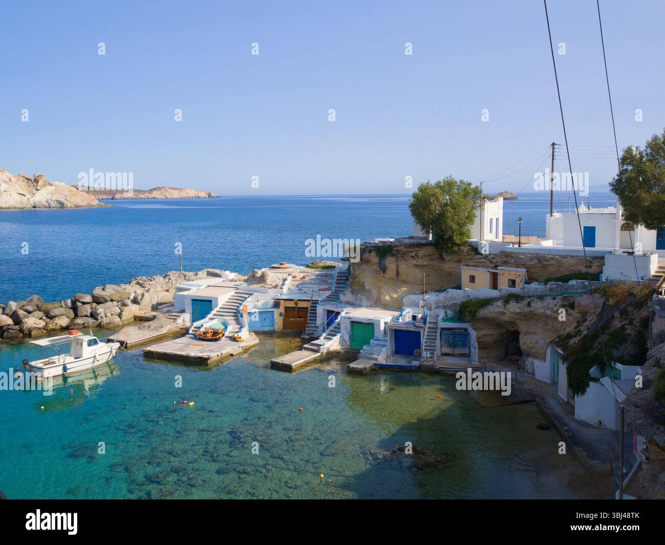 Tradizionali capanne da pesca con porte vivaci fiancheggiano le bianche scogliere di Mandrakia, Milos, che si innalzano sopra le calme acque turchesi. Foto Stock