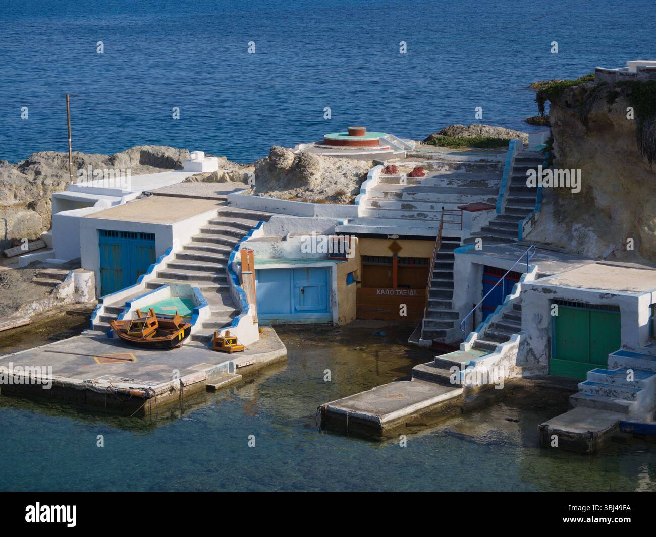 Una morbida foschia mattutina bagna le bianche scogliere e le colorate capanne del porto di Mandrakia e Milos con una luce delicata sopra l'acqua turchese. Foto Stock