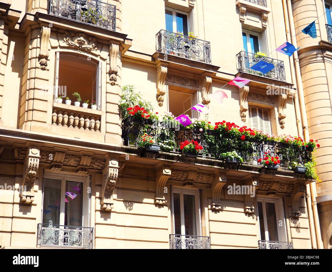 Facciata dell'edificio parigino con balconi pieni di fiori e bandiere festive Foto Stock