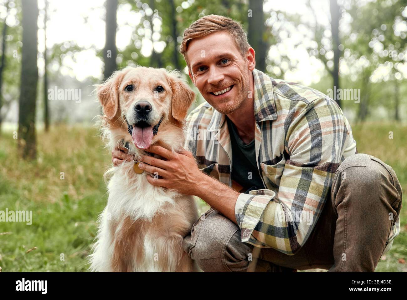 Un uomo allegro gode di un momento delizioso con il suo giocoso Golden retriever in una foresta lussureggiante, catturando gioia e compagnia nella natura, ideale per animali domestici Foto Stock