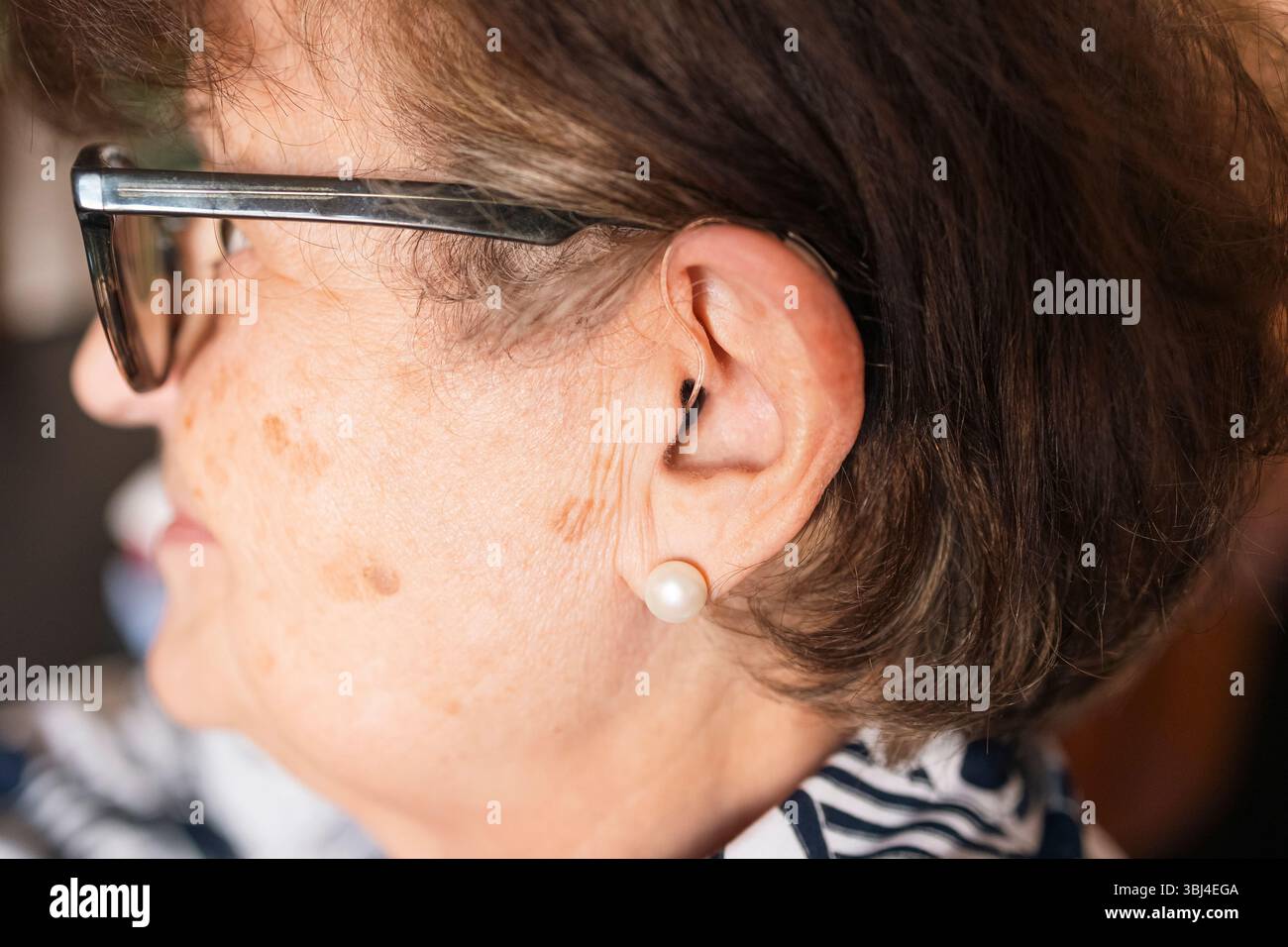 Primo piano di una donna anziana che indossa un apparecchio acustico e occhiali, evidenziando la tecnologia assistiva per la perdita dell'udito Foto Stock