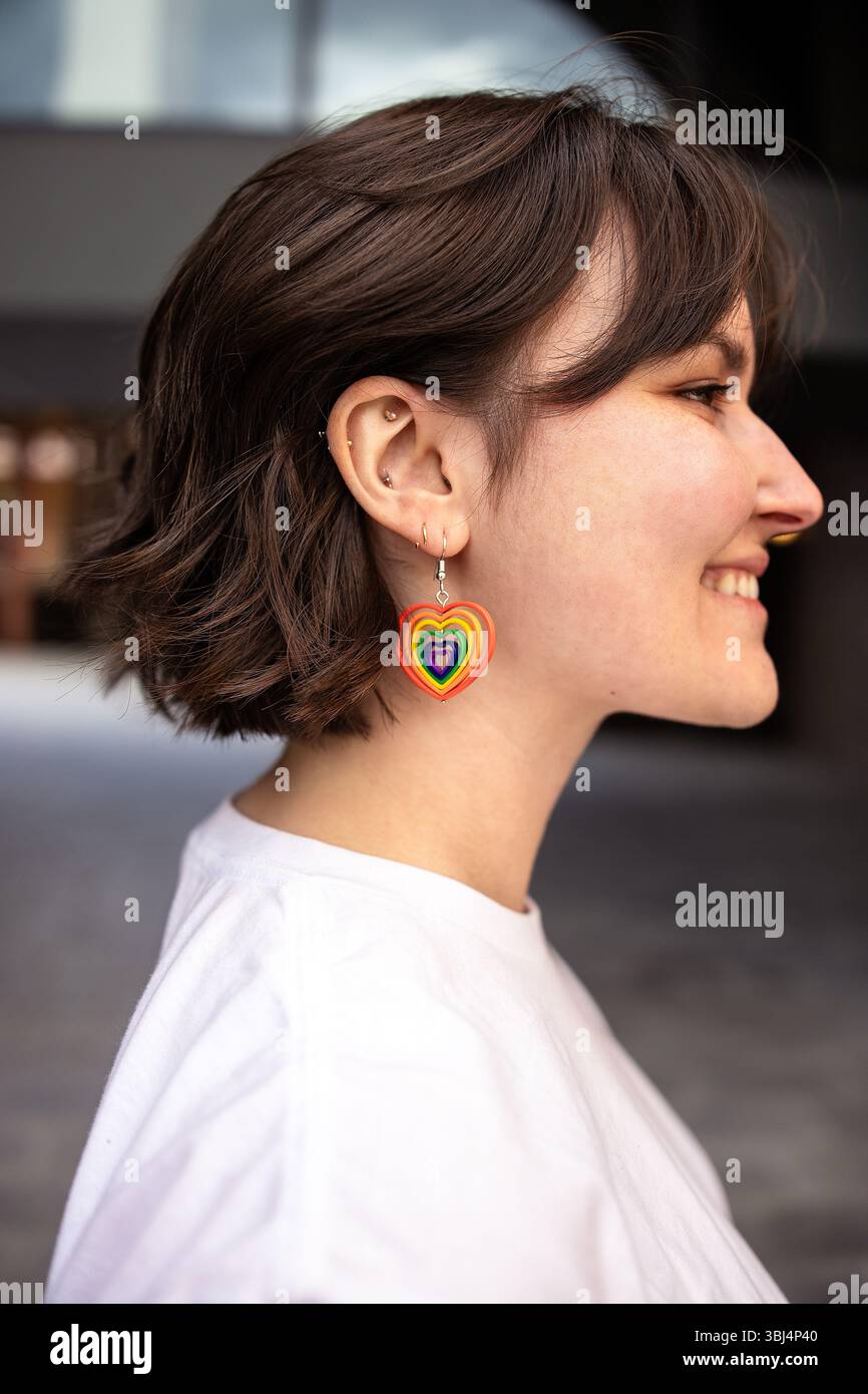 profilo di una donna con capelli corti che indossa orecchini arcobaleno Foto Stock