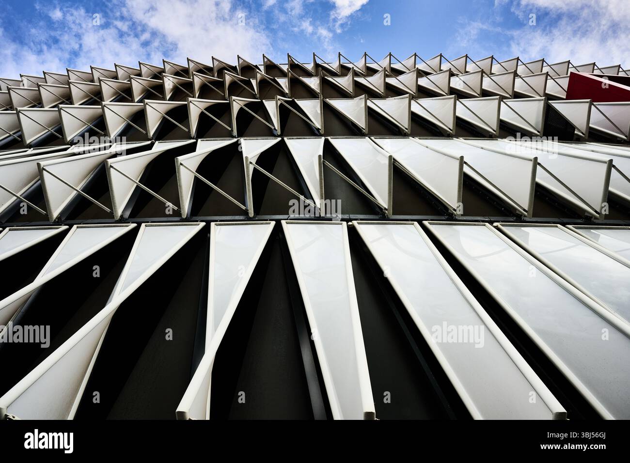 Finestre con sfumature triangolari bianche che creano uno schema dinamico sulla facciata di un edificio contemporaneo, che mostra un design architettonico innovativo Foto Stock
