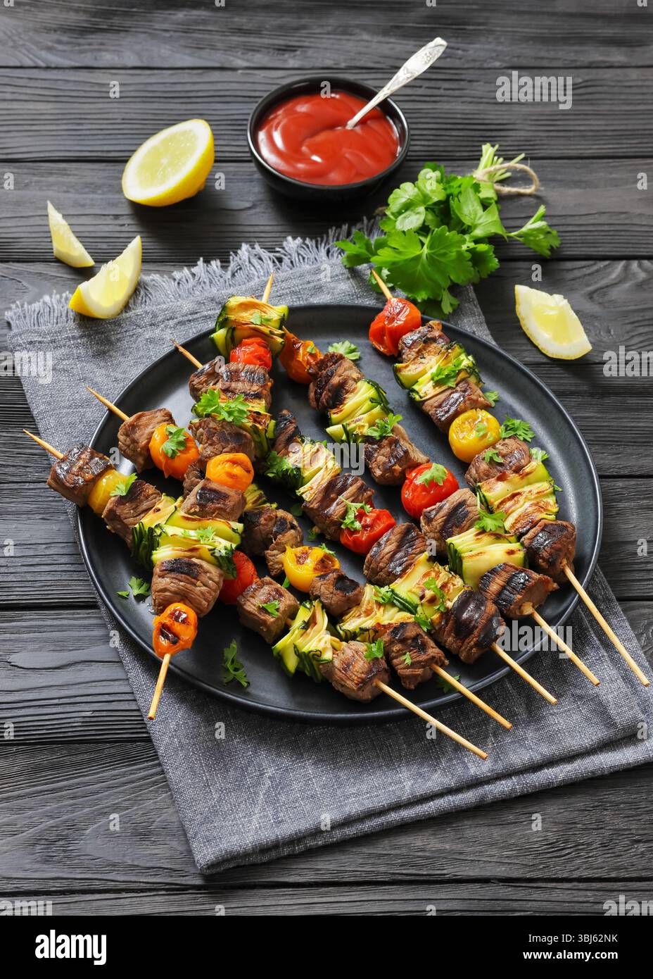 spiedini di manzo grigliati con verdure su un piatto, sfondo rustico scuro sul tavolo, foto vera per contenuti culinari e alimentari Foto Stock