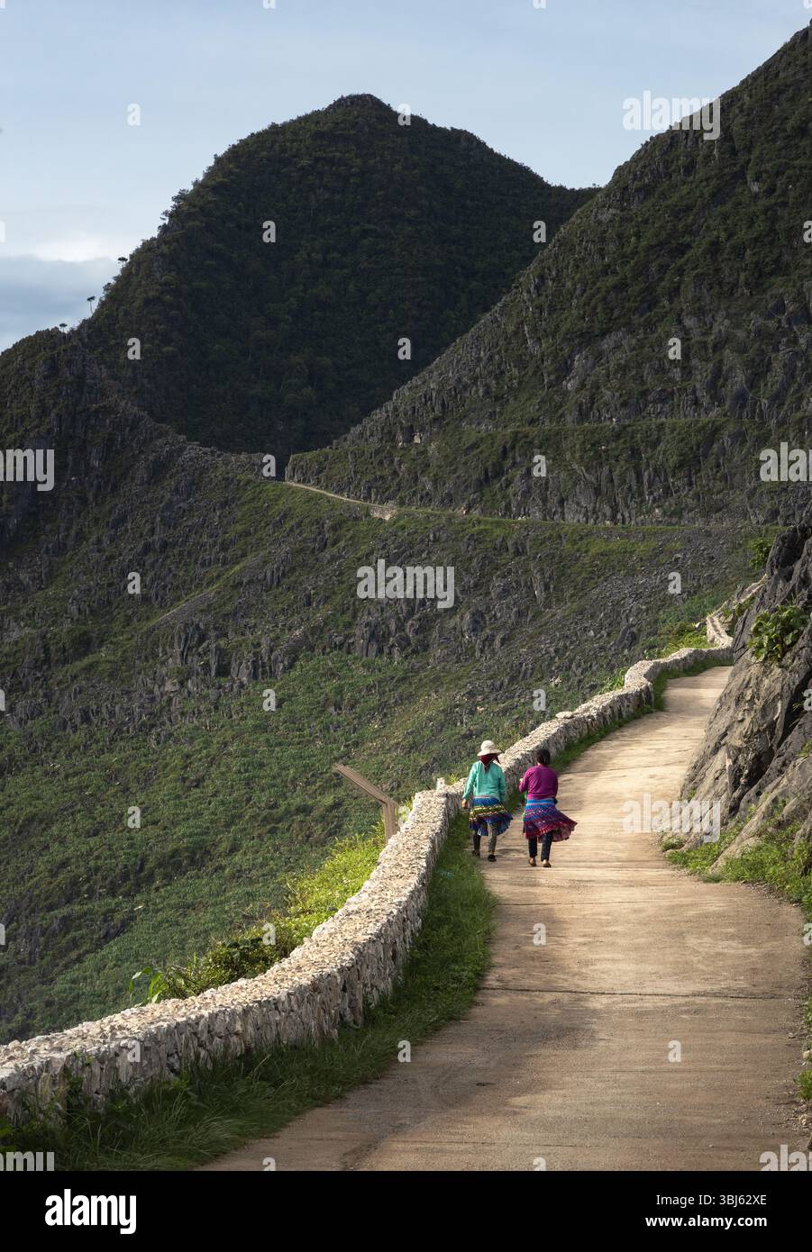 Due donne del posto in abiti tradizionali camminano lungo il passaggio sopraelevato ai margini della montagna Foto Stock
