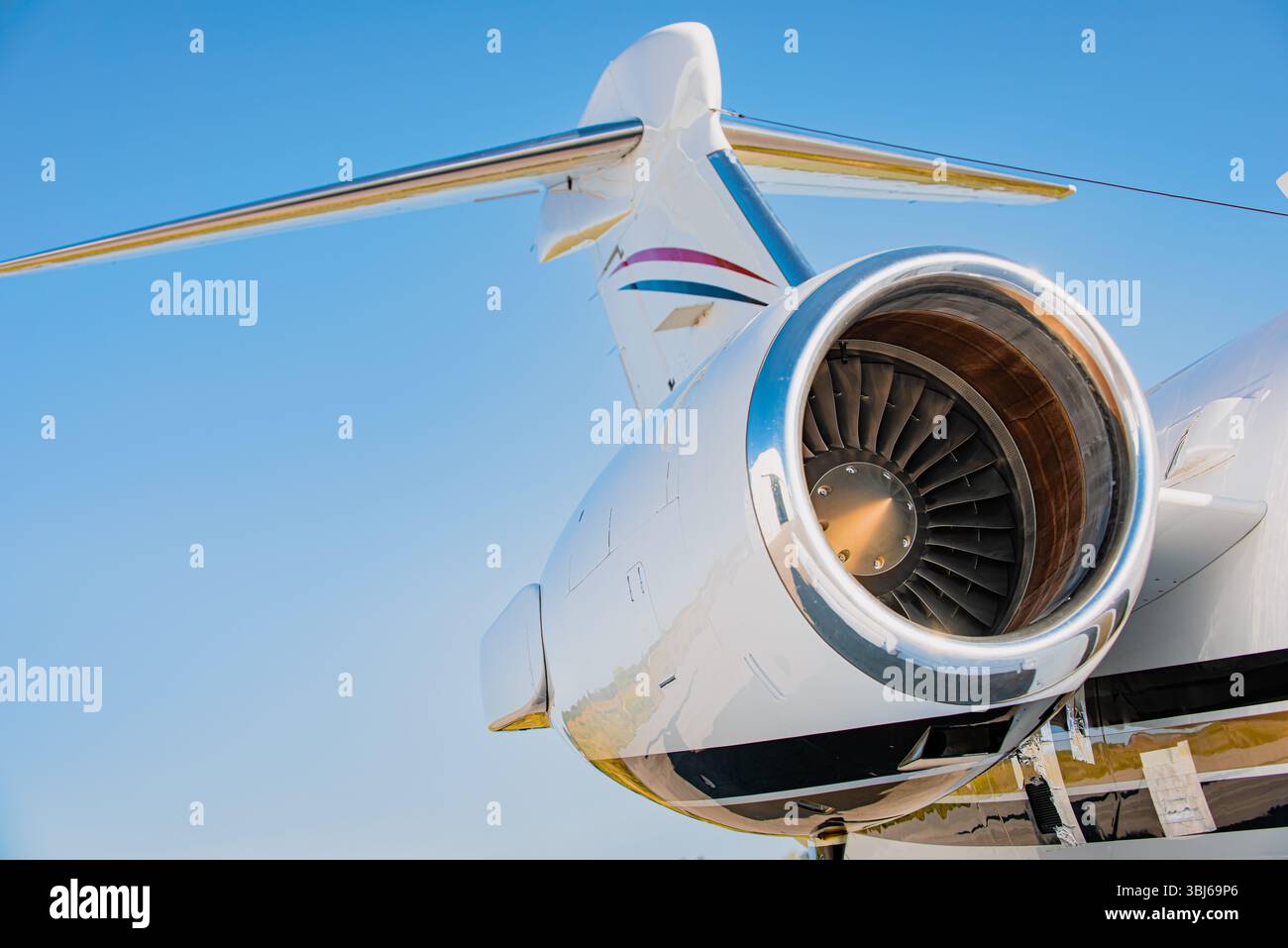 Primo piano del motore turbofan su aerei privati, coda e impennaggio visibili contro il cielo azzurro. Business jet su asfalto alla luce del sole. Foto Stock