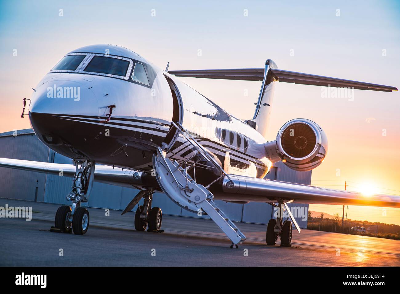Jet privato parcheggiato sull'asfalto all'alba, scale degli aerei dispiegate e hangar sullo sfondo. Business jet Gulfstream all'aeroporto executive. Foto Stock