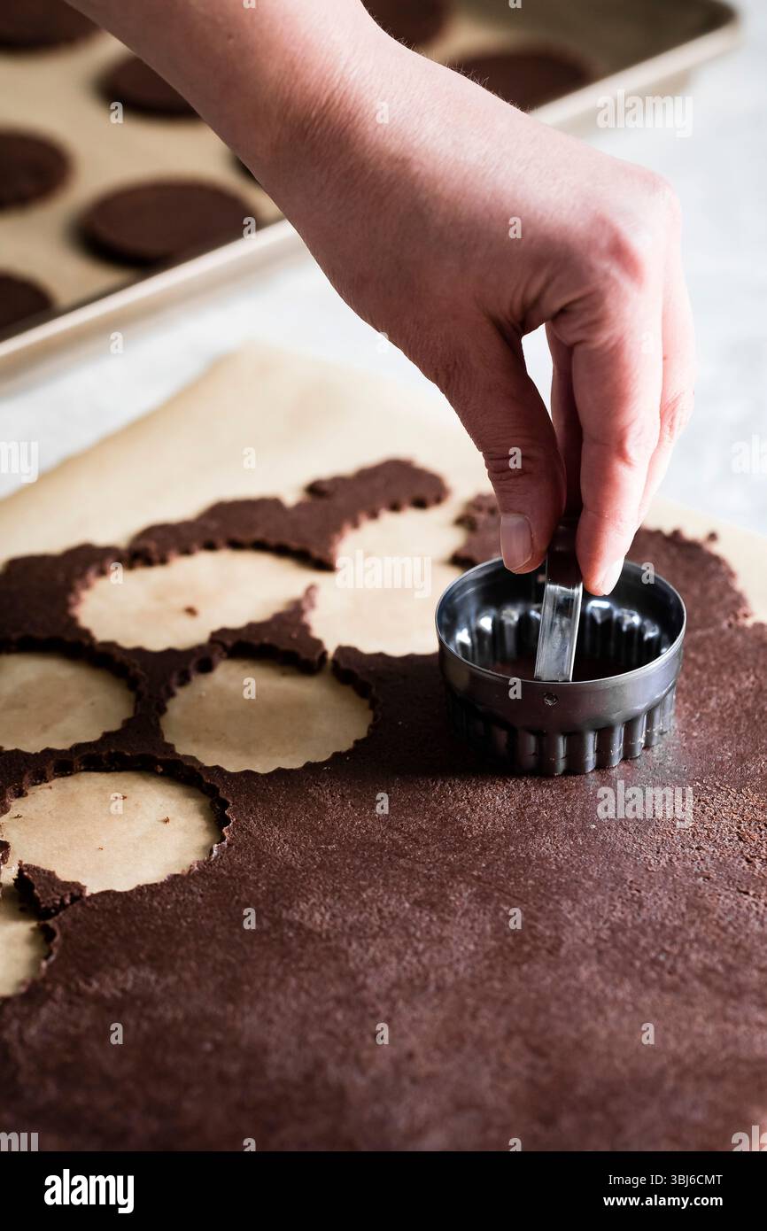 Una persona utilizza una forchetta rotonda per tagliare le forme dall'impasto al cioccolato su carta pergamena. Foto Stock