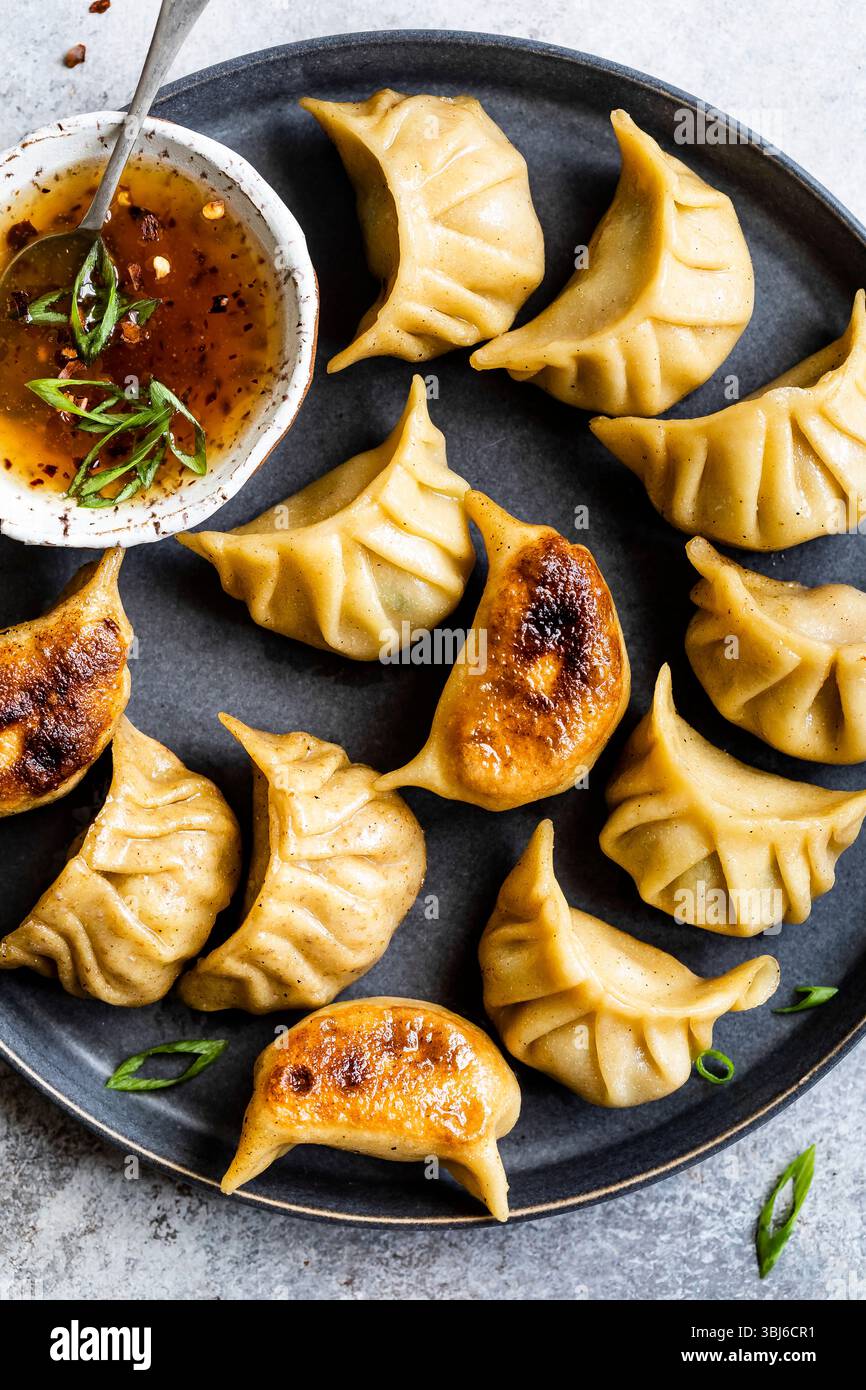 Un piatto di gnocchi fritti servito con una ciotola di salsa da immersione guarnita con cipolle verdi. Foto Stock