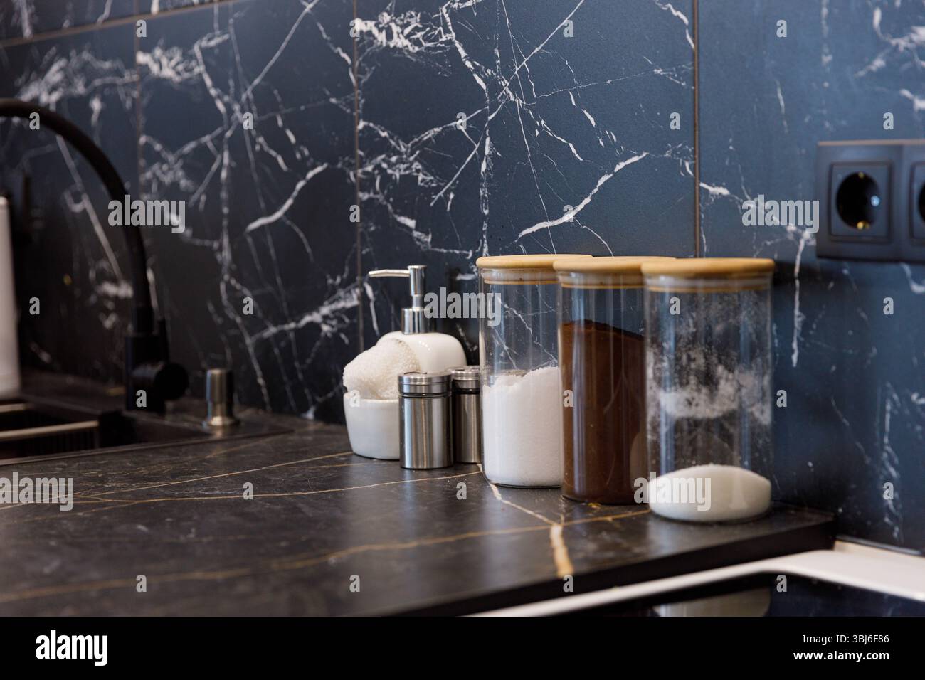 Un moderno piano di appoggio della cucina presenta un elegante design a parete in marmo, adornato da vasetti di vetro pieni di vari ingredienti, tra cui zucchero e spezie, Foto Stock
