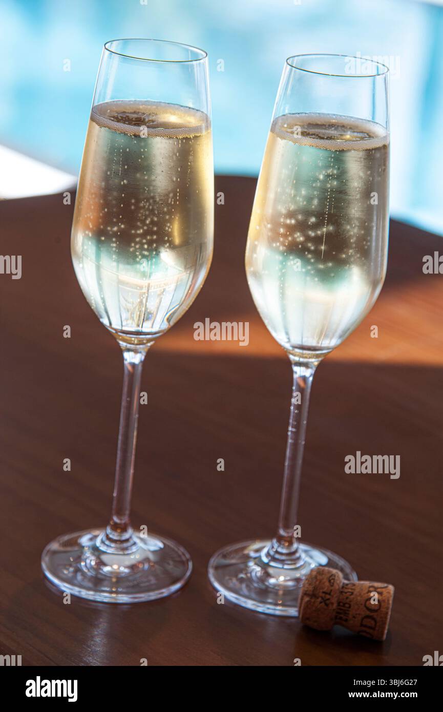 VACANZA DI LUSSO con champagne due bicchieri di spumante appena versati con sughero sul tavolo all'aperto della terrazza piscina dell'hotel villa vacanze sullo sfondo Foto Stock